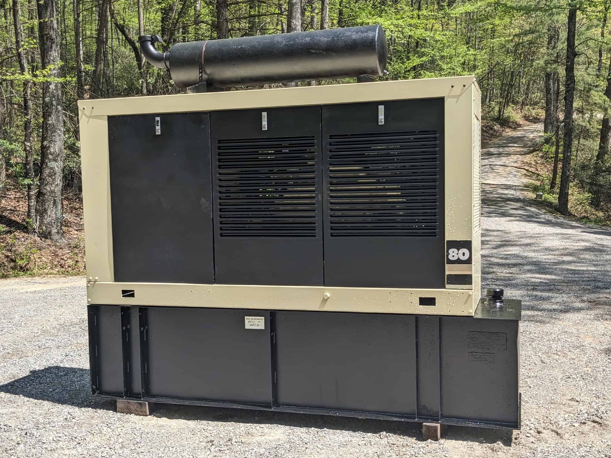 A refurbished industrial generator set placed outdoors, surrounded by trees, ready for operation.